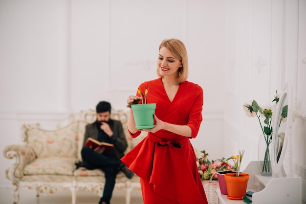 Notion de printemps. Une femme sensuelle tient une fleur de printemps pendant que l'homme lit un livre sur un canapé. Prenez soin des fleurs au printemps. Joyeux premier jour de printemps