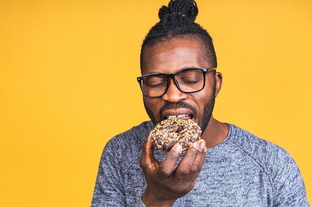 Photo notion de régime. homme barbu noir afro-américain affamé mangeant un beignet isolé sur fond jaune. malbouffe.