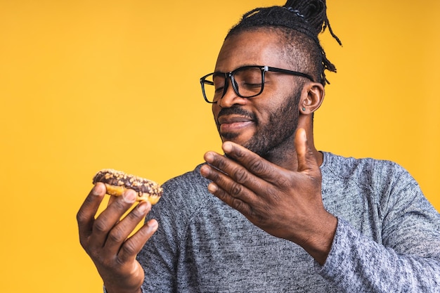 Notion de régime. Homme barbu noir afro-américain affamé mangeant un beignet isolé sur fond jaune. Malbouffe.