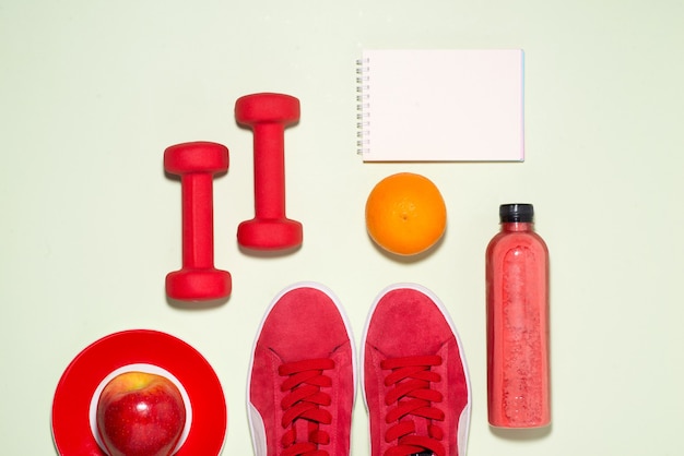 Notion de remise en forme. Baskets, pomme, haltère et bouteille de jus de fruits sur fond de couleur pastel.