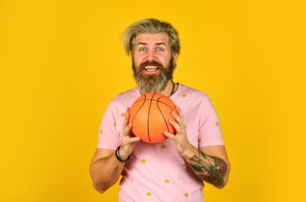 Notion de sport. Profitez du jeu. Jouez avec un ballon de basket. Heureux homme jouant. Passe-temps et loisirs. Mode de vie sain. Mec actif. Joueurs de basket-ball sur fond jaune. Joueur de basket-ball hipster.