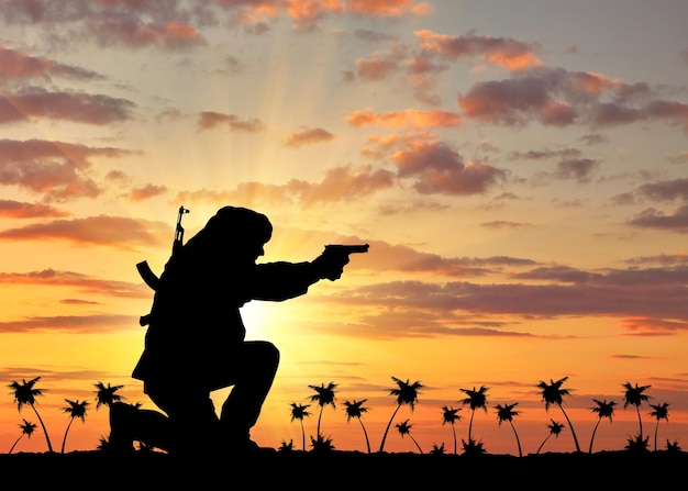 Notion de terrorisme. Silhouette d'un terroriste avec un fusil sur fond de coucher de soleil et de palmiers