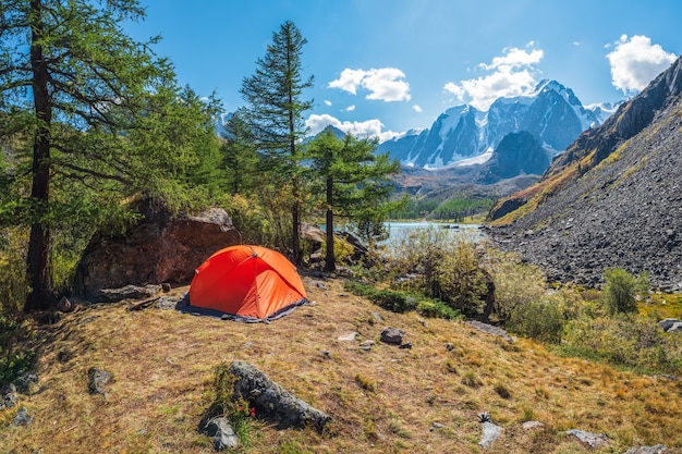 Notion de tourisme. Tente solitaire dans la forêt de montagne. Tente de camping orange sur le rivage au soleil.