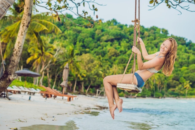 Notion de vacances. Heureuse jeune femme assise sur une balançoire, profitant d'une vue sur la mer