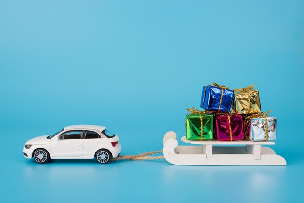 Notion de vacances de Noël. La photo en gros de toy mini car transportant un traîneau en bois blanc plein de petits coffrets isolés sur fond bleu