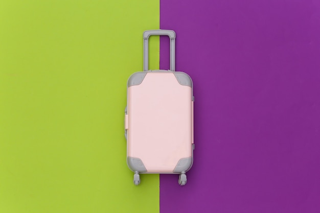 Notion de voyage. Mini valise de voyage en plastique sur fond violet vert. Style minimaliste. Vue de dessus, mise à plat
