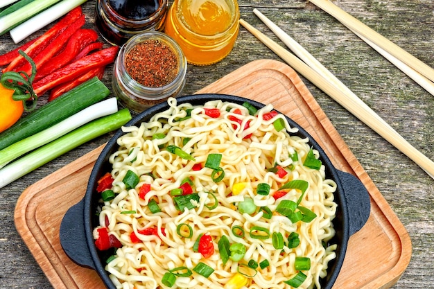 Nouilles à la chinoise dans une poêle en fonte sur un support en bois. Nouilles chinoises aux légumes et aux piments. Nouilles végétariennes épicées aux légumes.