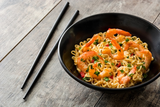 Nouilles et crevettes aux légumes dans un bol noir sur table en bois