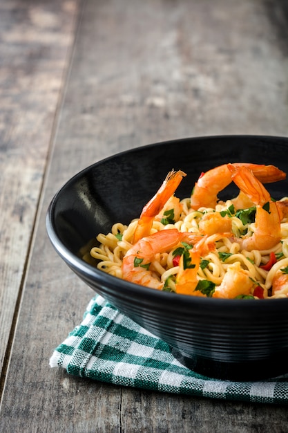 Nouilles et crevettes aux légumes dans un bol noir sur table en bois