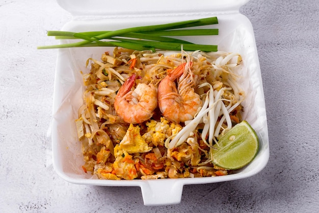 Nouilles frites à la thaïlandaise avec crevettes dans une boîte en mousse, Pad Thai avec des légumes tels que des oignons nouveaux, du citron vert, des germes de soja et du tofu. nourriture de rue populaire de Thaïlande, vue de dessus.