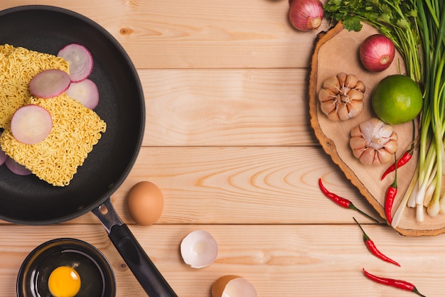 Nouilles instantanées pour cuisiner et manger dans le plat avec des œufs et des légumes sur fond de bois.