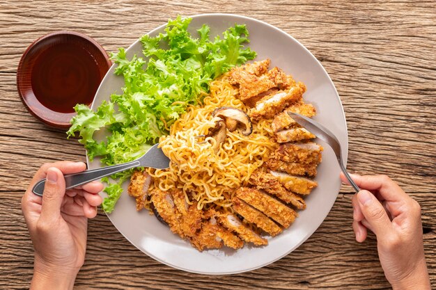 Nouilles Instantanées Sautées Avec Escalope De Porc Frite Japonaise Ou Tonkatsu, Laitue Et Champignons Shiitake à Côté De La Sauce Tonkatsu Garnie De Sésame Blanc Sur Fond De Texture Bois Rustique, Vue De Dessus