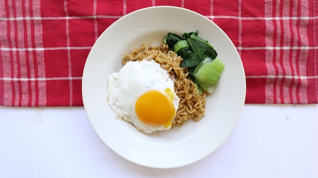 Photo nouilles instantanées servies avec des œufs frits et des légumes verts à la moutarde sur une assiette nouilles frites instantanées indomie