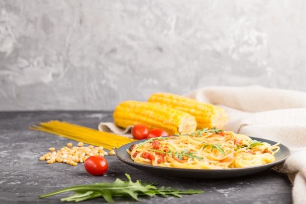 Nouilles de maïs avec sauce tomate et roquette sur fond de béton noir. Vue latérale, espace copie.