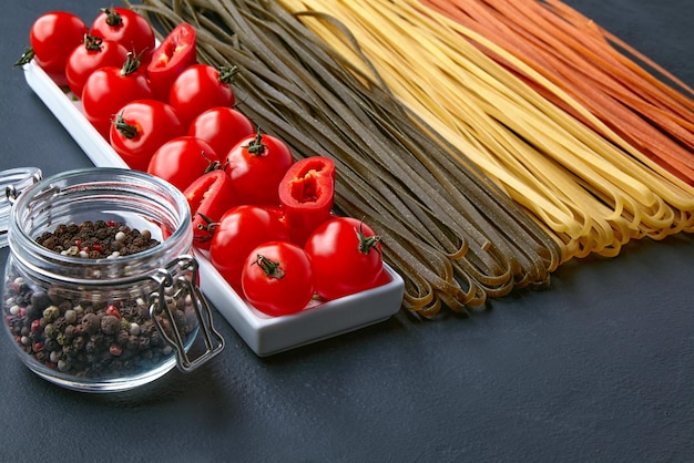 Nouilles maison de différentes couleurs à partir d'ingrédients végétaux naturels un bol oblong avec tomates et paprika rouge