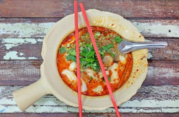 Nouilles de poisson épicé dans le bol avec des baguettes et une cuillère sur la table en bois.