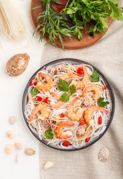 Nouilles de riz aux crevettes ou crevettes et petites pieuvres sur plaque en céramique grise sur un fond en bois blanc. Vue de dessus, gros plan.