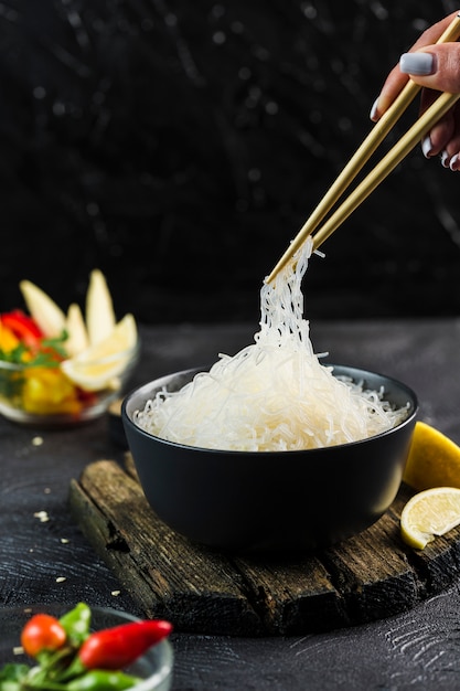 Nouilles de riz Cellophane aux légumes dans un bol noir avec des baguettes sur fond sombre, vue de côté agrandi.