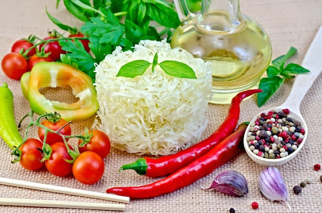 Nouilles de riz torsadées, tomates, poivre différent, huile en carafe, baguettes, ail sur fond de toile de sac