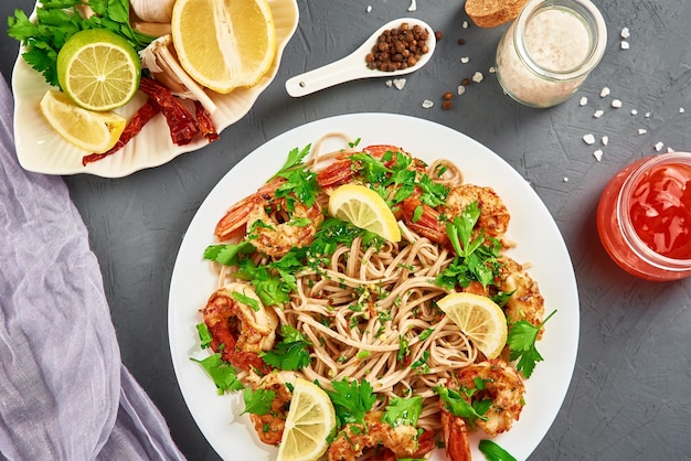 Nouilles sautées aux crevettes, citron et persil frais sur plaque blanche, soba aux crevettes, cuisine asiatique, vue de dessus