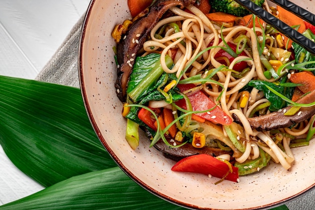 Nouilles sautées Udon avec viande de boeuf et légumes dans une assiette sur fond de bois blanc