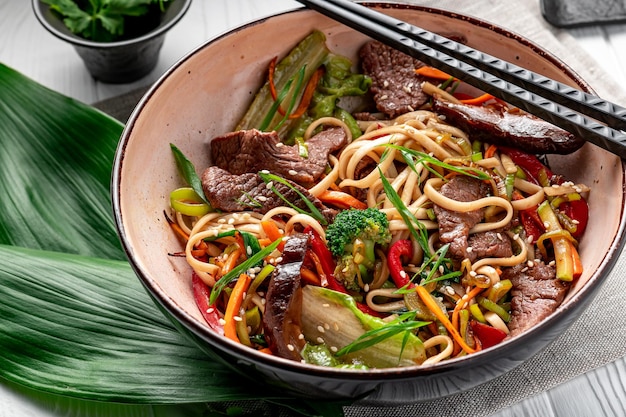 Nouilles sautées Udon avec viande de boeuf et légumes dans une assiette sur fond de bois blanc