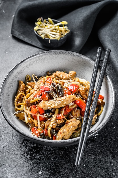 Nouilles sautées Udon à la viande de poulet et au sésame sur fond noir