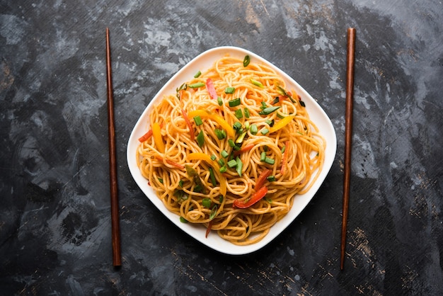 Les nouilles Schezwan ou les nouilles hakka aux légumes ou chow mein sont des recettes indochinoises populaires, servies dans un bol ou une assiette avec des baguettes en bois. mise au point sélective