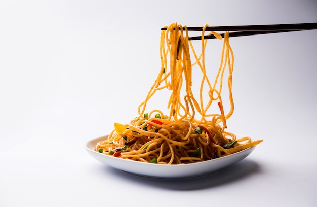 Les nouilles Schezwan ou les nouilles hakka aux légumes ou chow mein sont des recettes indochinoises populaires, servies dans un bol ou une assiette avec des baguettes en bois. mise au point sélective