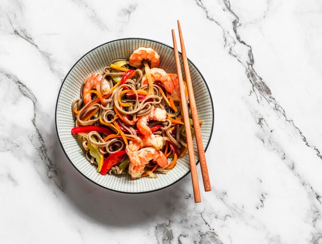 Nouilles soba aux légumes et crevettes sur fond clair vue de dessus