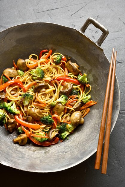 Des nouilles Udon frites avec des légumes dans une casserole sur fond de pierre noire