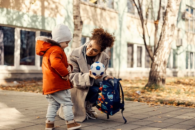 Une nounou veut jouer au foot ou au foot avec un petit garçon alors elle lui montre un ballon