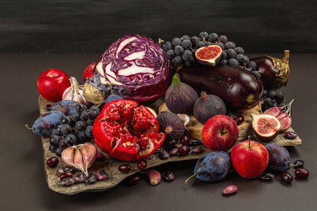 Nourriture bleue, rouge et violette. Arrière-plan culinaire de fruits et légumes. Figues fraîches, prunes, oignons, aubergines, raisins, choux, pommes, ail, cornouiller, grenade. Fond de pierre noire, mise à plat