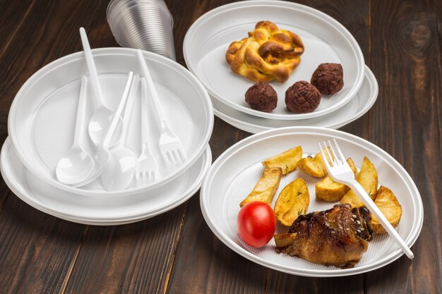 Nourriture dans la vaisselle en plastique blanc jetable. Prendre soin de l'environnement. Le problème est le recyclage. Table en bois. Vue de dessus