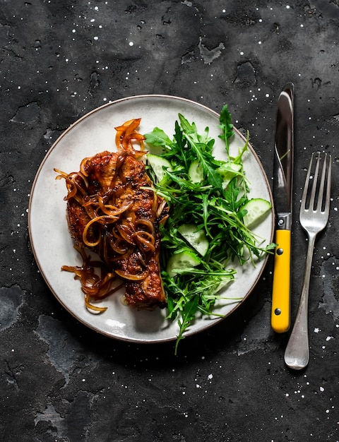 Nourriture délicieuse côtelette de porc barbecue grillée sur un os avec oignon caramélisé et salade de concombre de roquette sur fond sombre vue de dessus