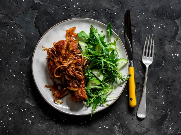 Nourriture délicieuse côtelette de porc barbecue grillée sur un os avec oignon caramélisé et salade de concombre de roquette sur fond sombre vue de dessus