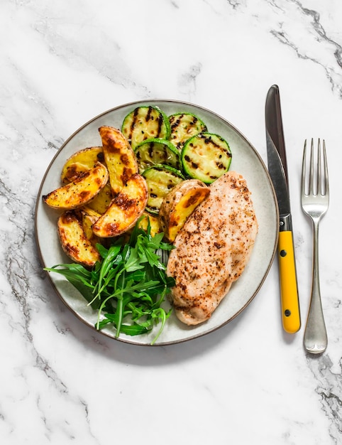 Nourriture délicieuse pommes de terre rôties poitrine de poulet courgettes grillées et salade d'épinards de roquette sur fond sombre vue de dessus