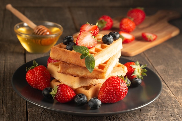 Nourriture fraîche faite maison de gaufres belges aux baies avec miel, chocolat, fraise, myrtille, sirop d'érable