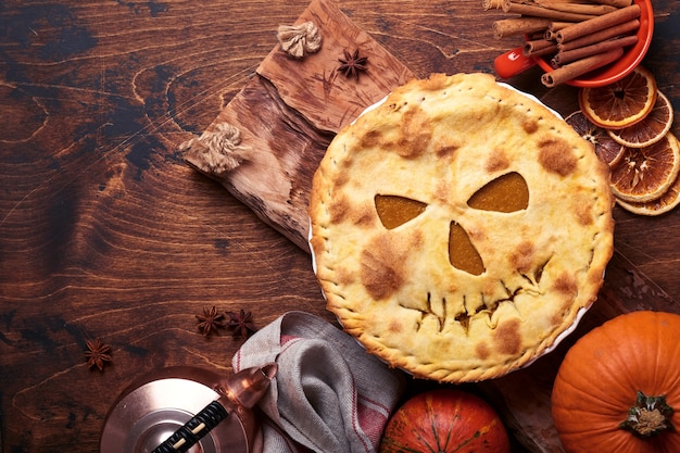 Nourriture d'Halloween. Tarte à la citrouille ou tarte maison avec un visage effrayant pour Halloween sur une table en bois. Espace de copie. Concept de nourriture d'Halloween.