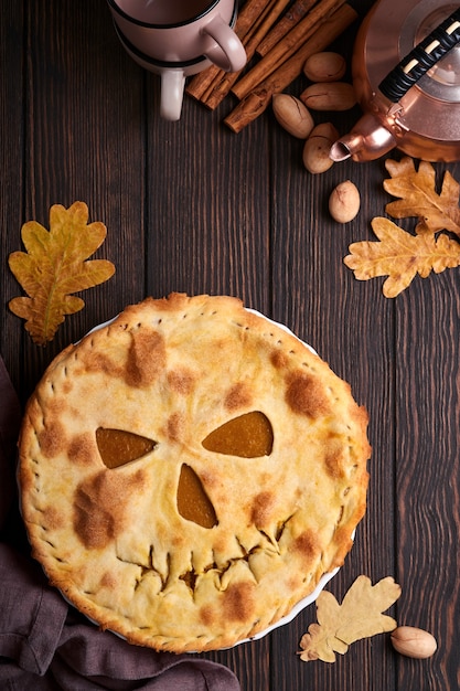 Nourriture d'Halloween. Tarte à la citrouille ou tarte maison avec un visage effrayant pour Halloween sur une table en bois. Espace de copie. Concept de nourriture d'Halloween.