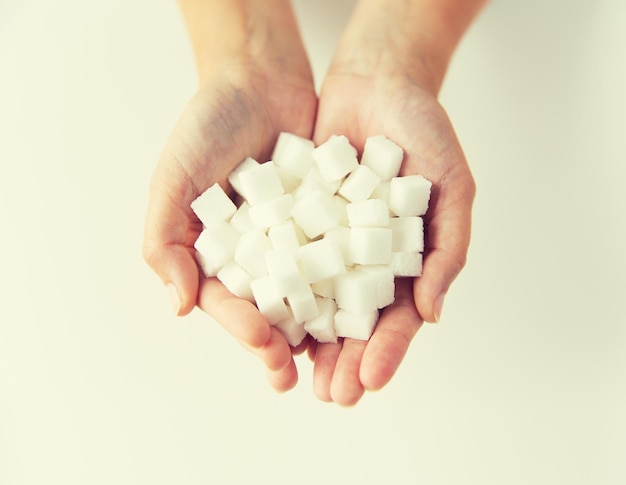 nourriture, junk-food, diabète et concept d'alimentation malsaine - gros plan d'un morceau de sucre blanc dans les mains d'une femme