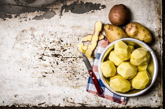 Photo nourriture de pomme de terre. les pommes de terre pelées dans un bol en métal sur la table rustique. espace libre pour le texte. vue de dessus