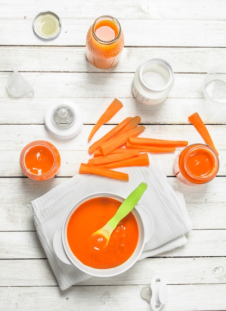 Nourriture pour bébés. Purée de carottes bébé avec du lait dans une bouteille. Sur une surface en bois blanche.