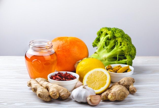 Nourriture pour la stimulation de l'immunité et la protection contre les virus. Brocoli, agrumes, miel, gingembre, citron, ail, goji, curcuma sur fond de bois blanc. Une alimentation saine et naturelle pour renforcer le système immunitaire