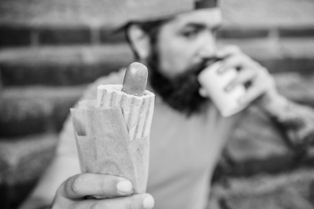 Nourriture de rue si bonne Nutrition de style de vie urbain Hipster insouciant manger de la malbouffe tout en étant assis dans les escaliers Collation d'homme affamé Malbouffe Mec mangeant un hot-dog Homme barbu mordant de délicieuses saucisses et buvant un gobelet en papier