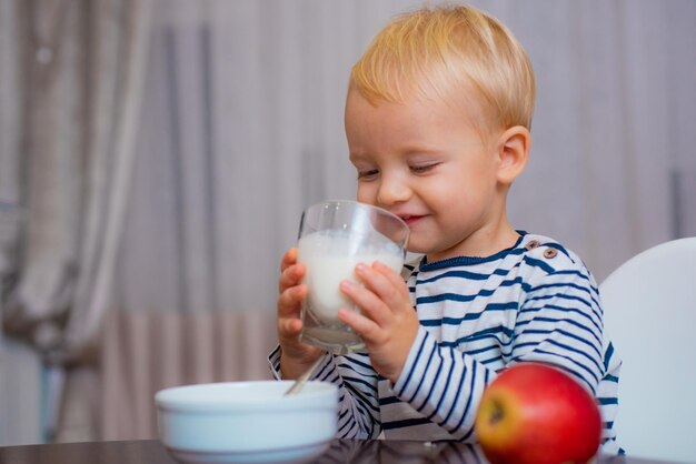 Nourriture saine Garçon mignon bébé prenant son petit déjeuner Nutrition pour bébé Manger sainement Tout-petit ayant une collation Alimentation saine Boire du lait Enfant tenir un verre de lait Enfant mignon garçon assis à table avec assiette et nourriture