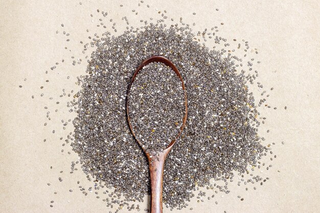 Photo nourriture saine graines de chia ou superaliments dans une cuillère en bois et tombant sur fond de texture en carton