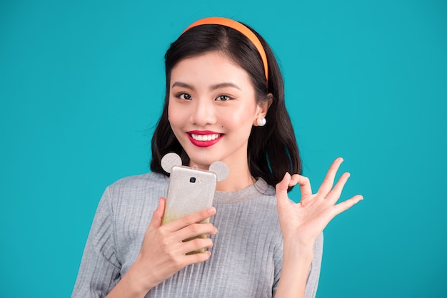 Nourriture saine. Gros plan sur une jolie fille asiatique pin-up souriante tenant un smartphone sur fond bleu.