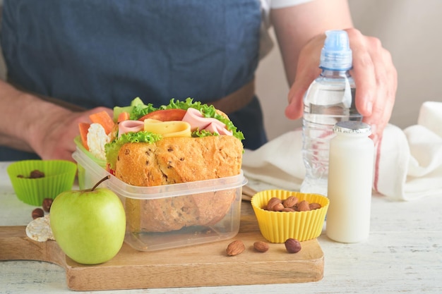 Nourriture saine pour le concept de déjeuner scolaire Père de soins faisant le déjeuner scolaire Sandwich avec pain sain viande fromage pomme concombre carottes noix eau yaourt dans un récipient Concept de retour à l'école