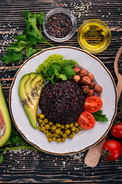 Nourriture saine Riz noir avocat tomates cerises pois verts et noisettes Sur un fond en bois Vue de dessus Espace libre pour votre texte